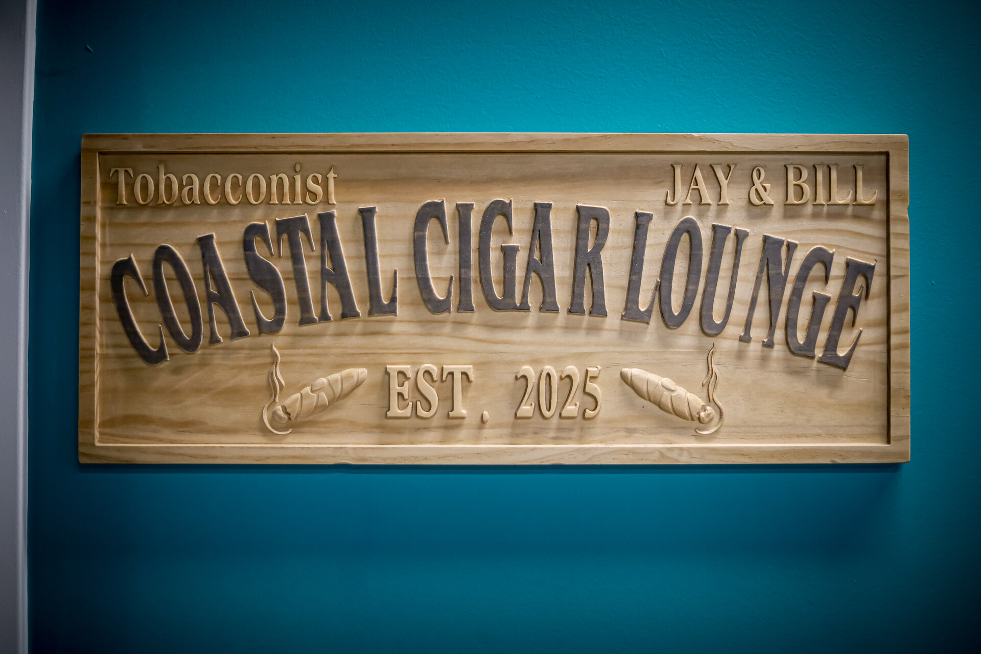 Wooden Coastal Cigar Lounge sign on an aqua wall